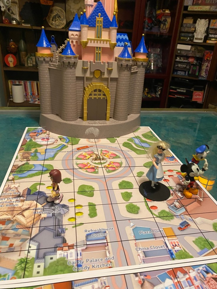 A gaming table with a Disneyland map on it, leading to a toy Disneyland castle with several Disney toys on it.